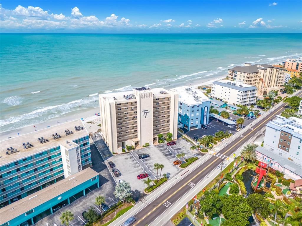 An aerial view shows a multi-story beachfront hotel building with a parking lot and road — 19450 GULF BOULEVARD UNIT 203, INDIAN SHORES, FL
