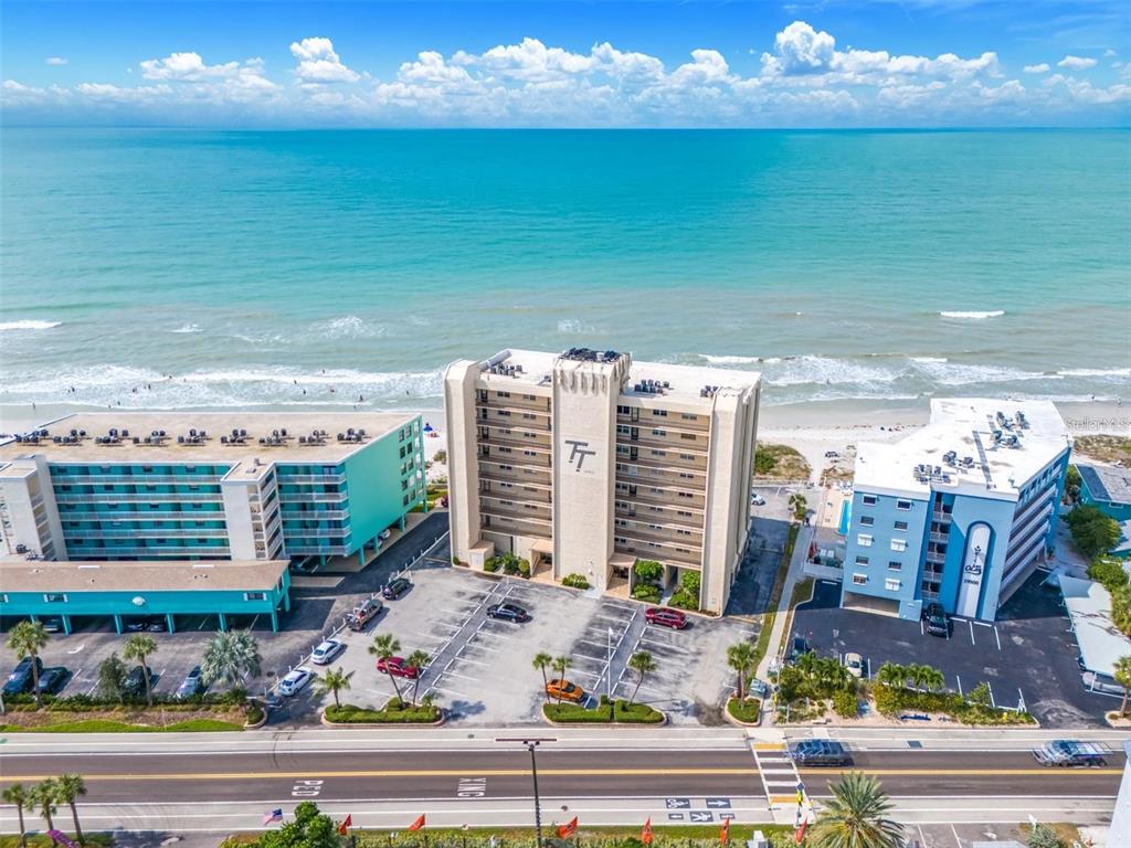 An aerial view shows three beachfront buildings with parking lots along a coastal road — 19450 GULF BOULEVARD UNIT 203, INDIAN SHORES, FL