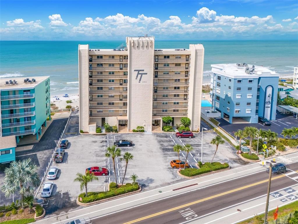 An aerial view shows a multi-story beachfront condominium building with a parking lot in front — 19450 GULF BOULEVARD UNIT 203, INDIAN SHORES, FL