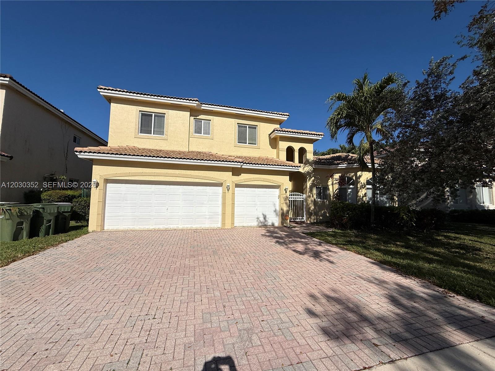 A two-story yellow stucco house features a three-car garage and a brick paver driveway — 2250 SE 19th Ave, Homestead FL 33035, HOMESTEAD, FL