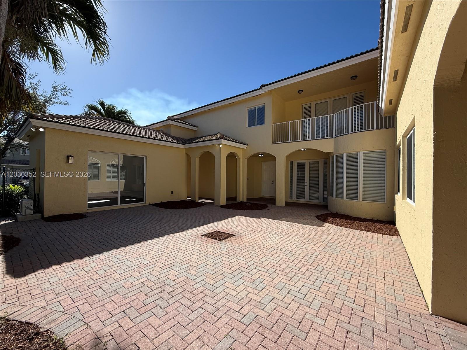 A paved courtyard sits before a two-story yellow house with a balcony and arched entryways — 2250 SE 19th Ave, Homestead FL 33035, HOMESTEAD, FL