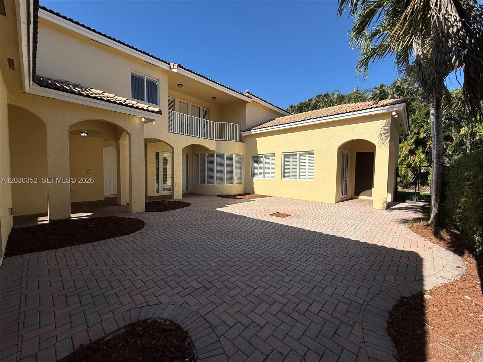 A two-story yellow stucco house features a paved courtyard and a second-floor balcony — 2250 SE 19th Ave, Homestead FL 33035, HOMESTEAD, FL