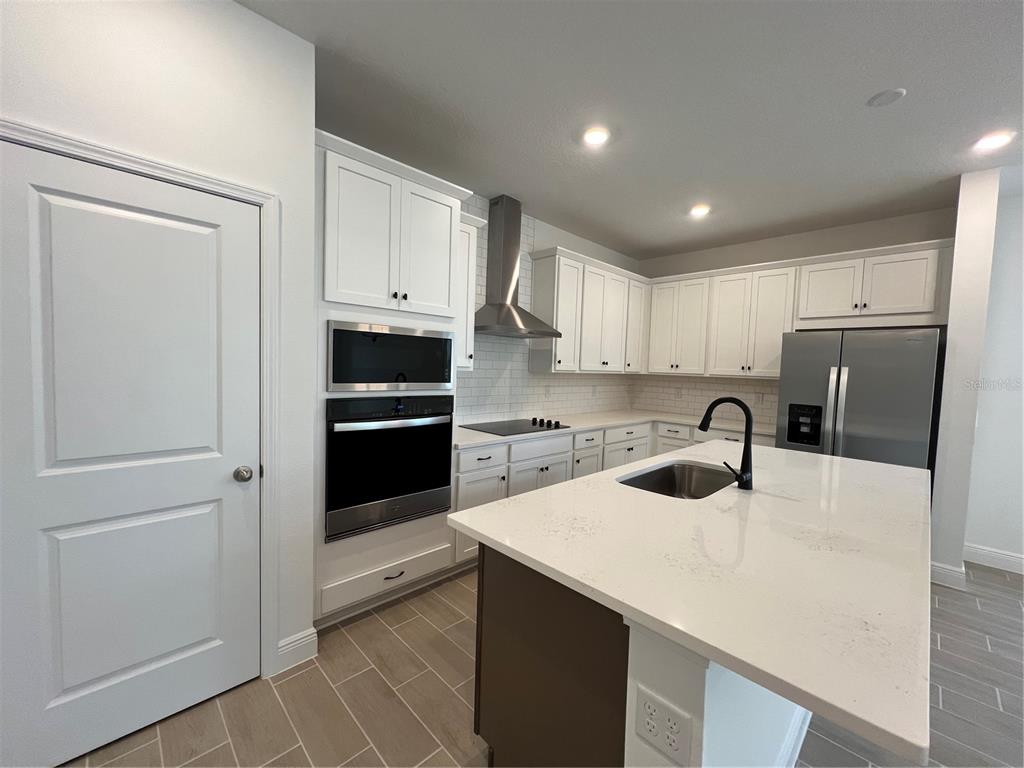 A modern kitchen features white cabinetry, stainless steel appliances, a center island, and tile flooring — 2213 JUNIPER BERRY AVENUE, MINNEOLA, FL