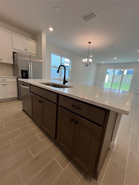 A kitchen island with a sink and dark cabinets sits before a stainless steel refrigerator — 2213 JUNIPER BERRY AVENUE, MINNEOLA, FL