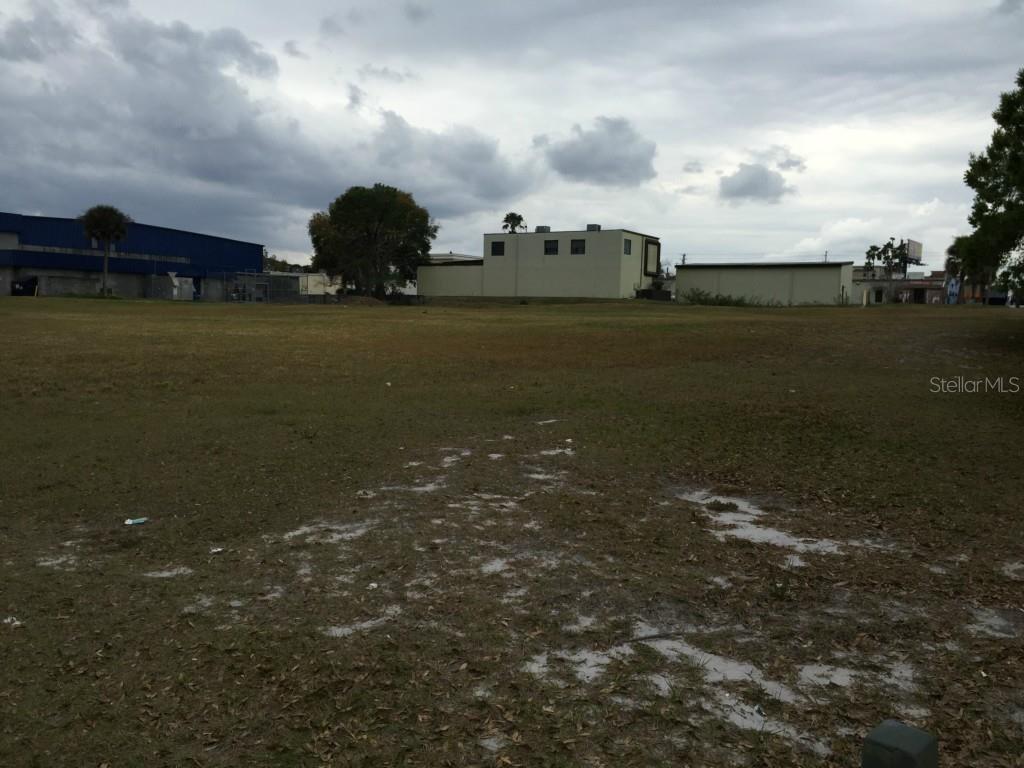 A large, flat, grassy vacant lot sits in front of several industrial buildings under cloudy skies — 6440 CANADA AVENUE, ORLANDO, FL
