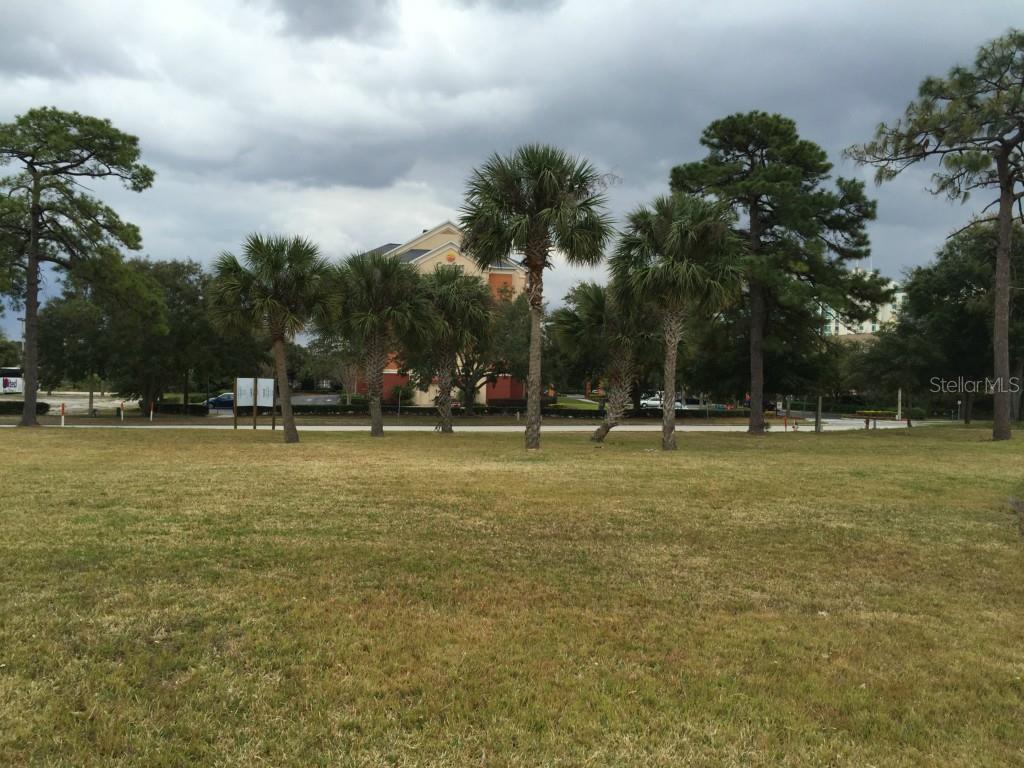 A grassy field with palm trees and pine trees in front of a hotel building — 6440 CANADA AVENUE, ORLANDO, FL