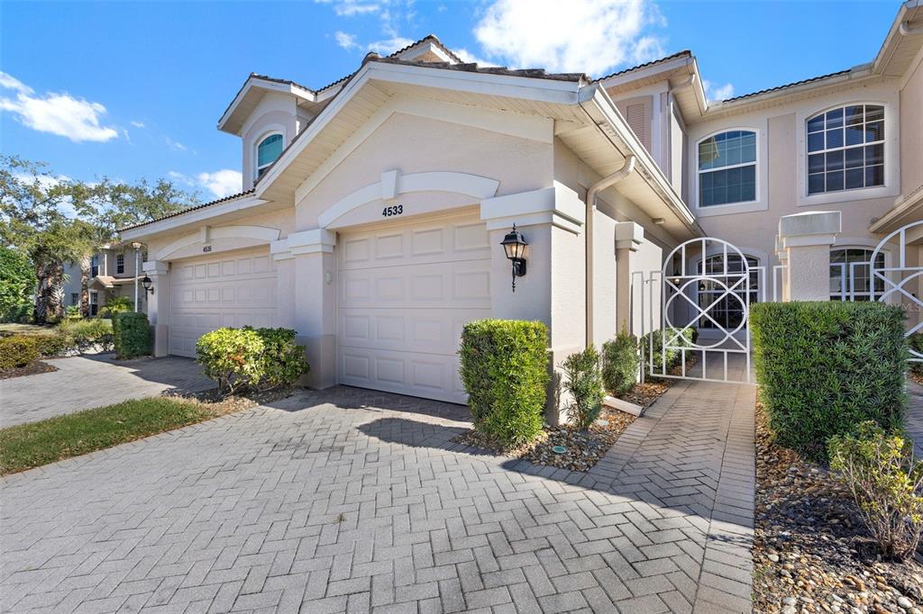 The exterior of a two-story townhouse features a paved driveway, two garage doors, and landscaping — 4533 CINNAMON DRIVE UNIT 2707, SARASOTA, FL