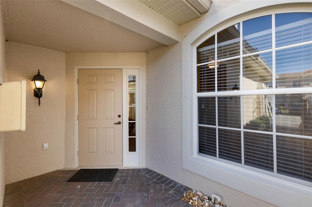 A tan front door with a side window sits on a brick porch beside a window — 4533 CINNAMON DRIVE UNIT 2707, SARASOTA, FL