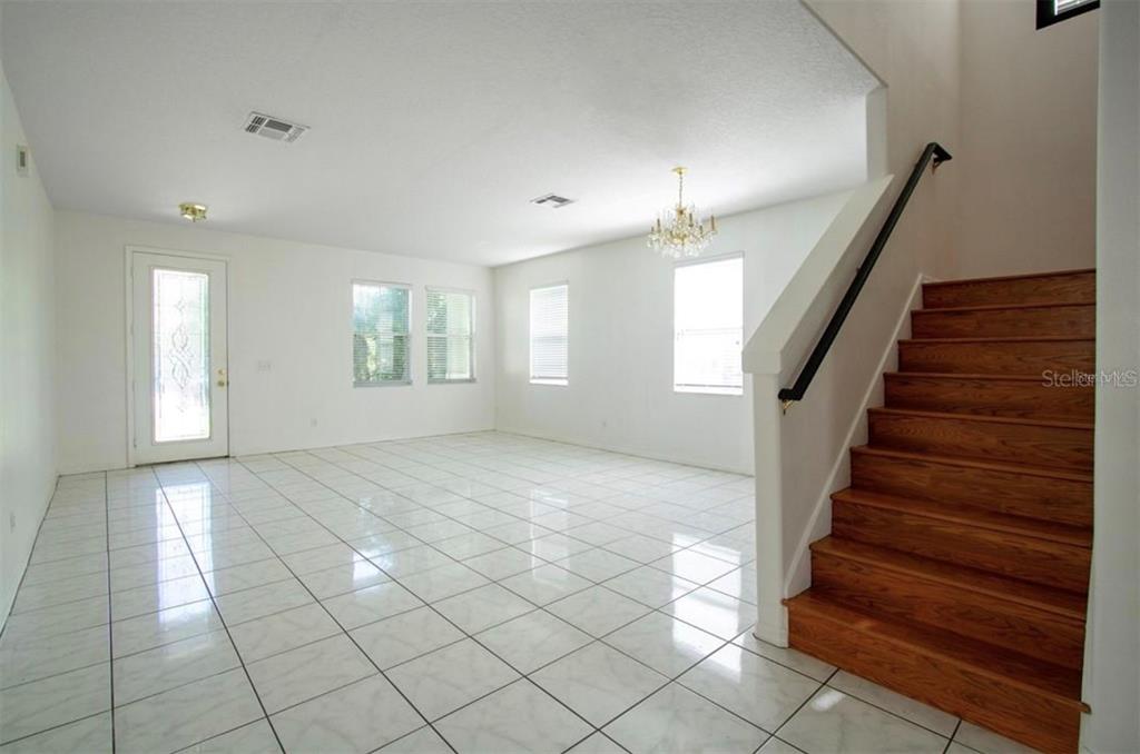 A bright, tiled living room features a wooden staircase with a black handrail — 1412 BLACKWATER POND DRIVE, ORLANDO, FL