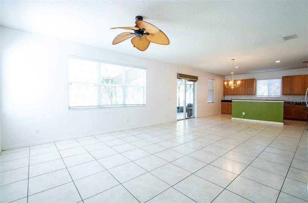 A spacious living area with white tile floors, a ceiling fan, and an adjacent kitchen — 1412 BLACKWATER POND DRIVE, ORLANDO, FL
