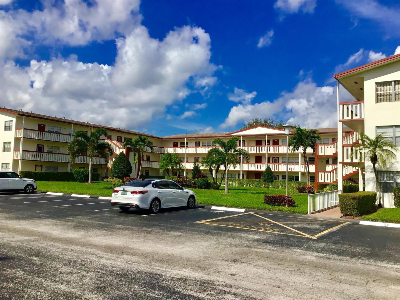 A white sedan is parked in front of a multi-story apartment complex with palm trees — 336 Brighton H # 336, Boca Raton FL 33434, BOCA RATON, FL