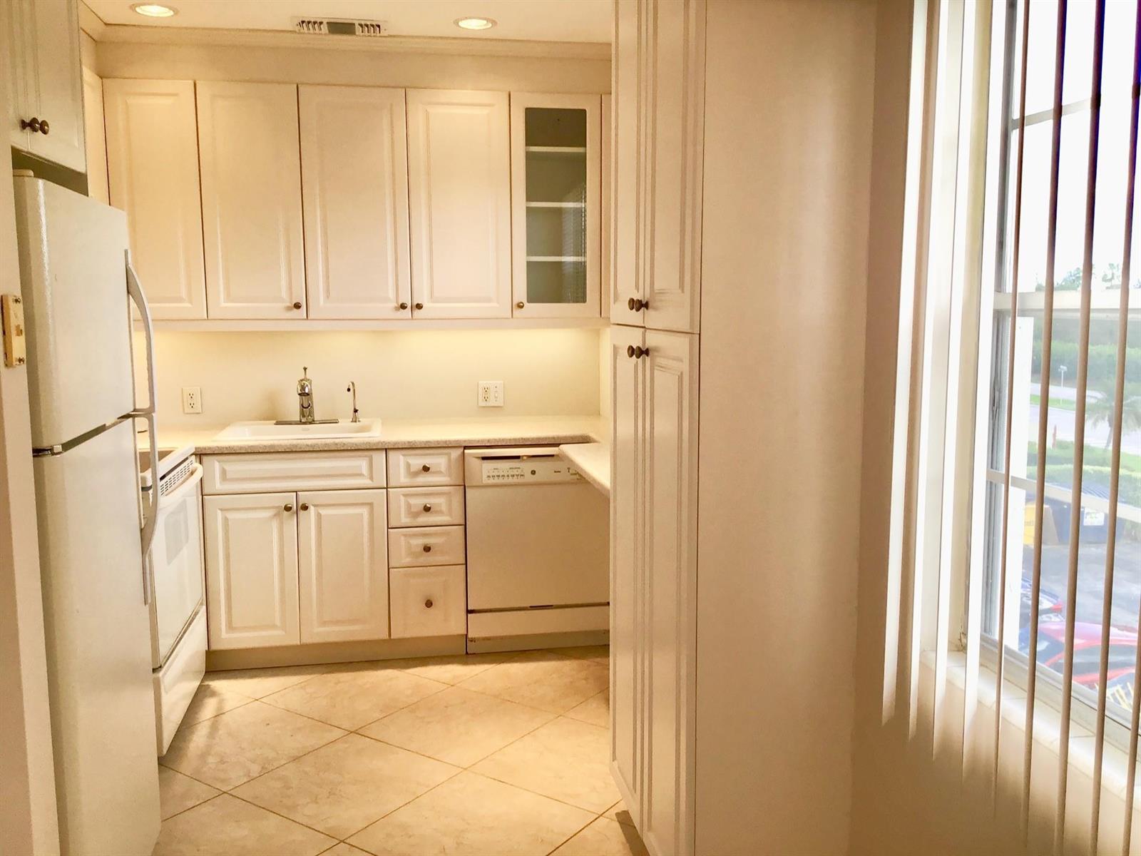 A kitchen features white cabinets, light countertops, tile flooring, and a window with vertical blinds — 336 Brighton H # 336, Boca Raton FL 33434, BOCA RATON, FL