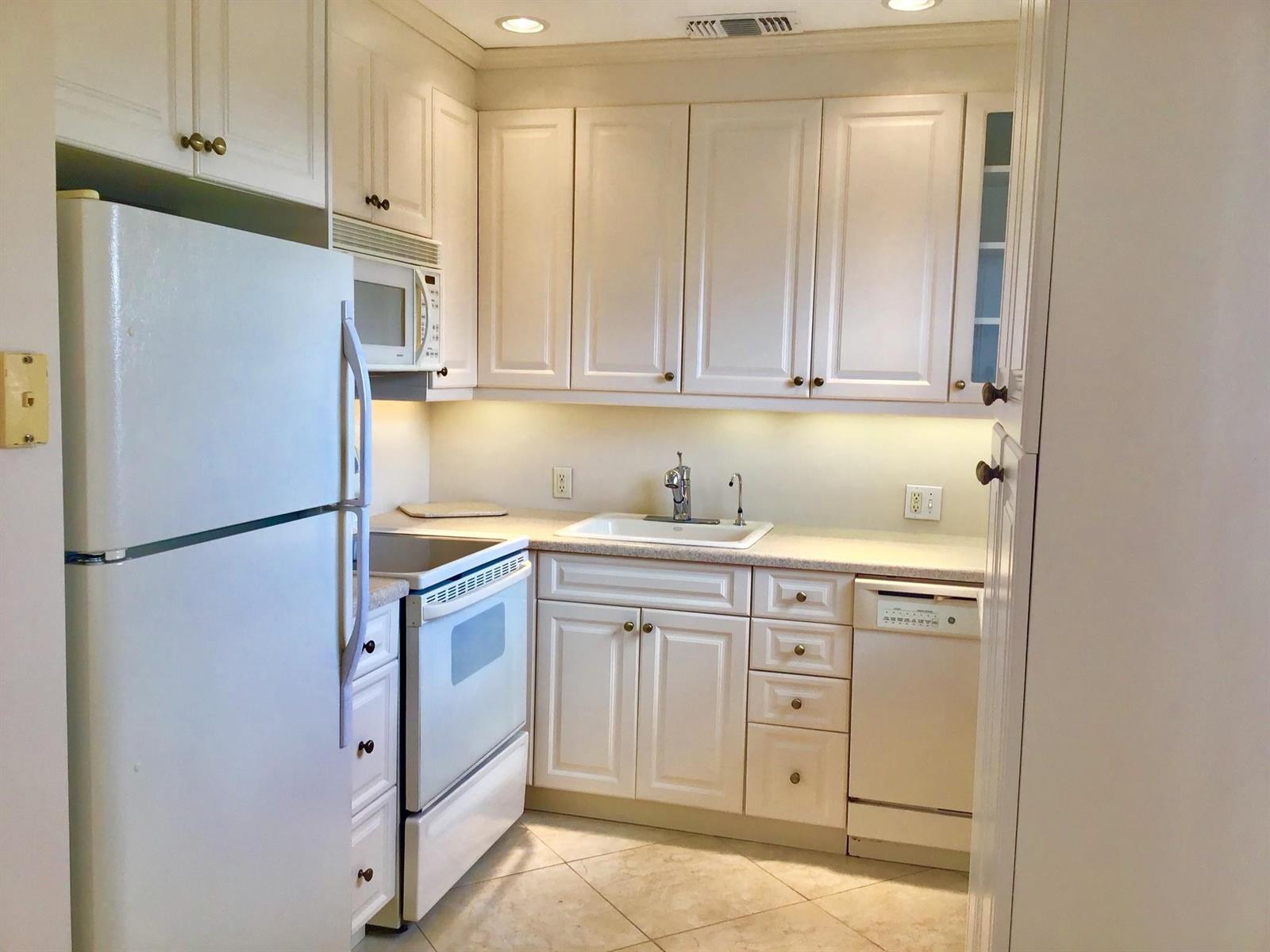 A small kitchen features white cabinets, white appliances, a sink, and light-colored tile flooring — 336 Brighton H # 336, Boca Raton FL 33434, BOCA RATON, FL