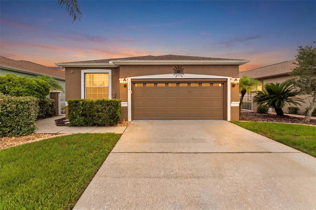 A single-story house with a brown stucco exterior, a two-car garage, and a concrete driveway — 7606 BERNA LANE, LAND O LAKES, FL