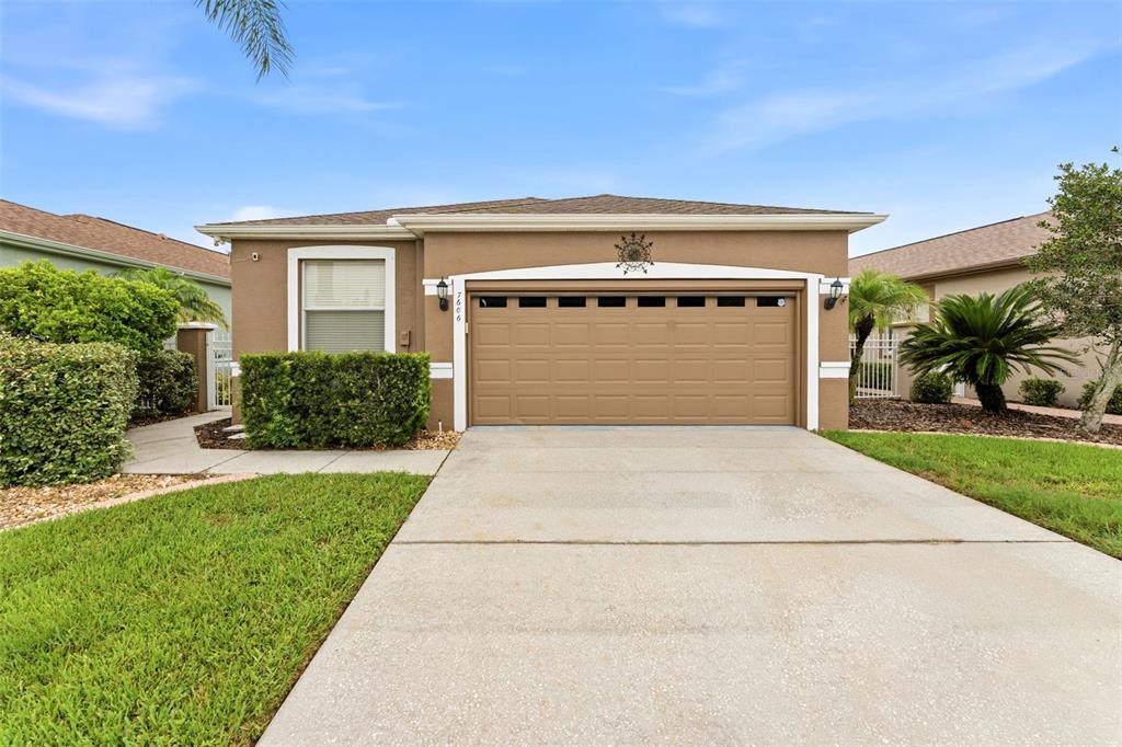A single-story house features a tan stucco exterior, a two-car garage, and a concrete driveway — 7606 BERNA LANE, LAND O LAKES, FL