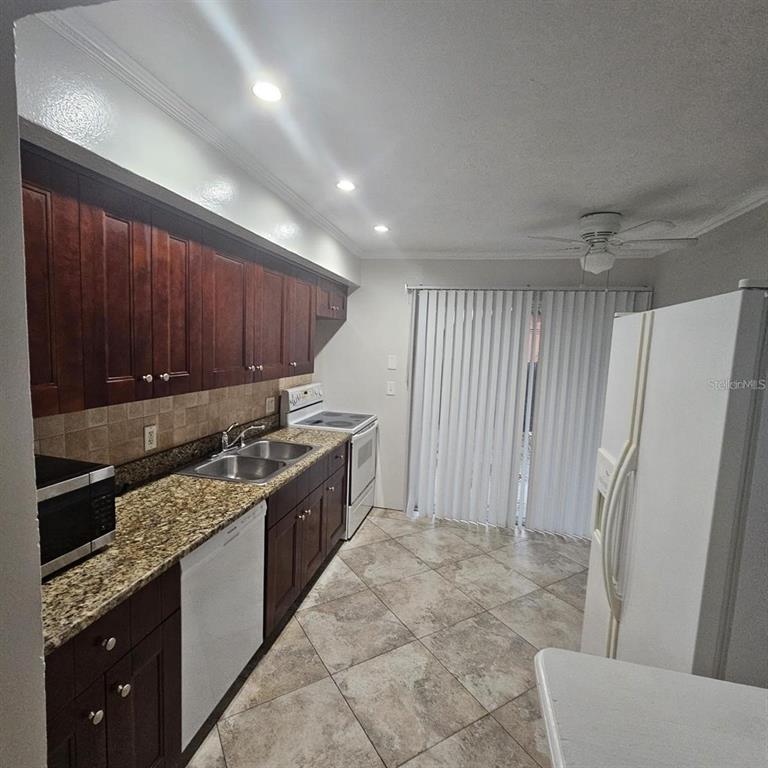 A kitchen features dark wood cabinets, granite countertops, tile flooring, and a white refrigerator — 5103 34TH STREET W, BRADENTON, FL
