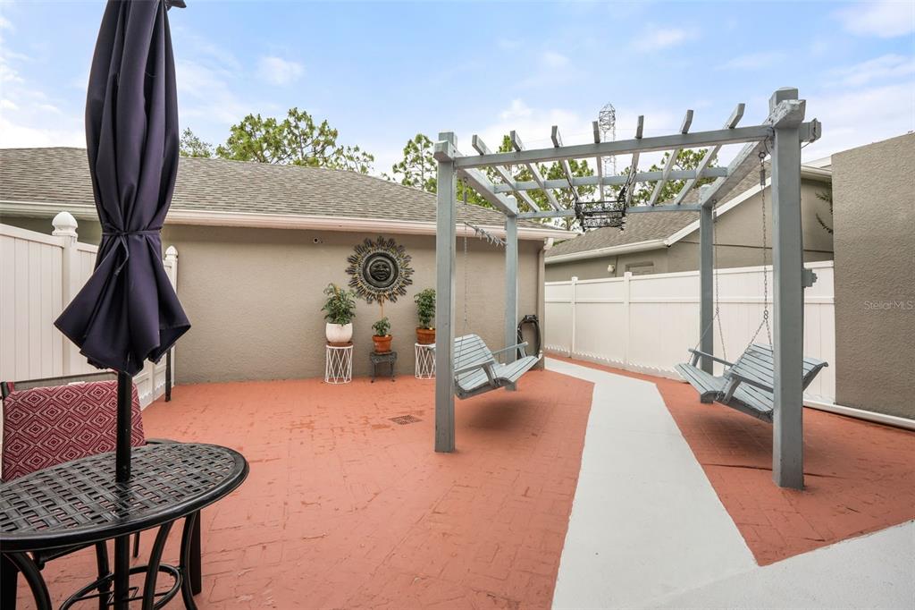 A patio features a pergola with two hanging benches, a dining table, and potted plants — 14432 CLARKSON DRIVE, ORLANDO, FL