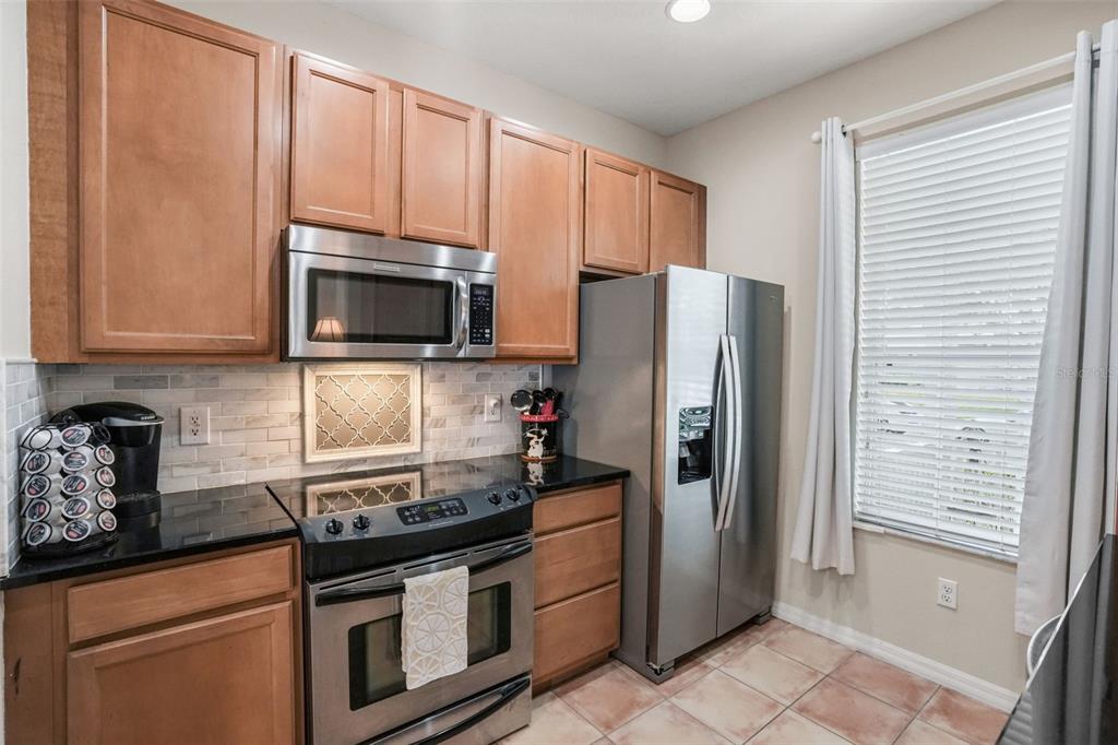 A kitchen features wood cabinets, stainless steel appliances, black countertops, and a tiled backsplash — 14432 CLARKSON DRIVE, ORLANDO, FL