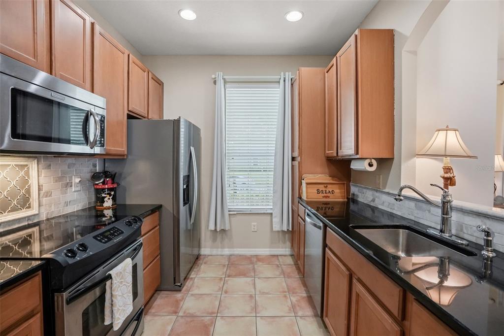 A galley kitchen features wood cabinets, black countertops, stainless steel appliances, and tile flooring — 14432 CLARKSON DRIVE, ORLANDO, FL