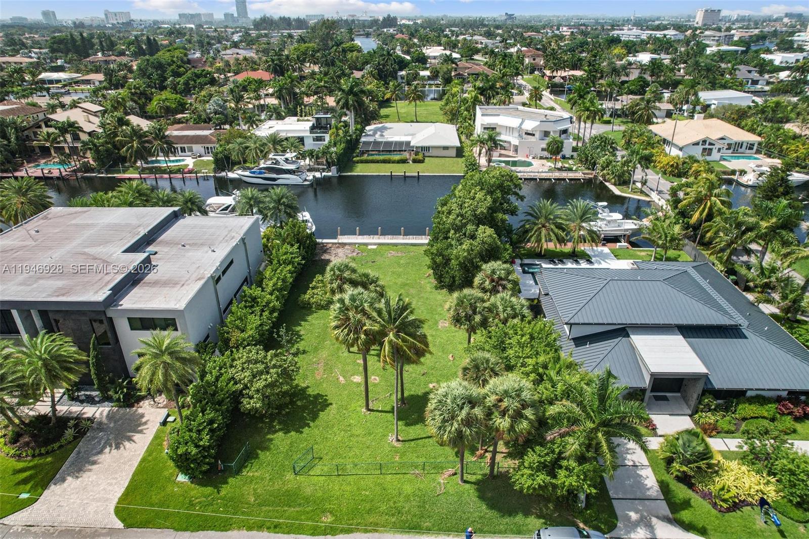 An aerial view shows a vacant grassy lot situated between two modern waterfront homes — 606 Palm Dr, Hallandale Beach FL 33009, HALLANDALE BEACH, FL