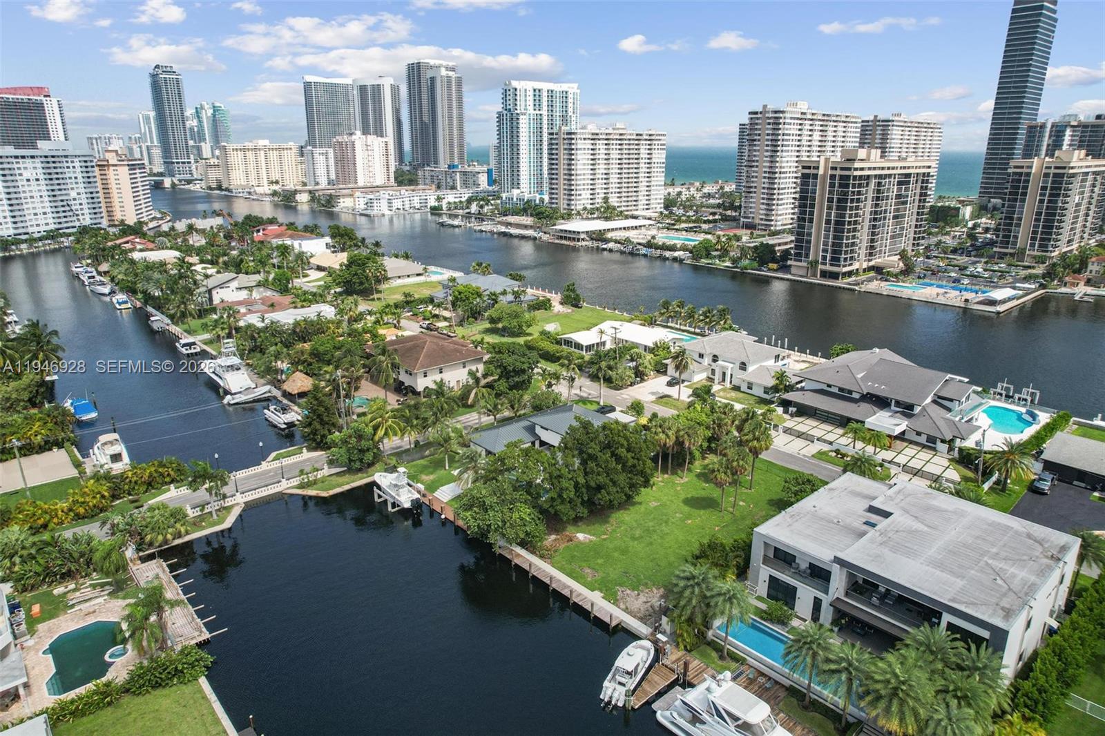 An aerial view shows waterfront homes with private docks and pools near a city skyline — 606 Palm Dr, Hallandale Beach FL 33009, HALLANDALE BEACH, FL