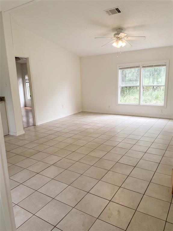 An empty room with white walls, tiled flooring, a ceiling fan, and a large window — 3296 LAKE BUFFUM ROAD W, FORT MEADE, FL