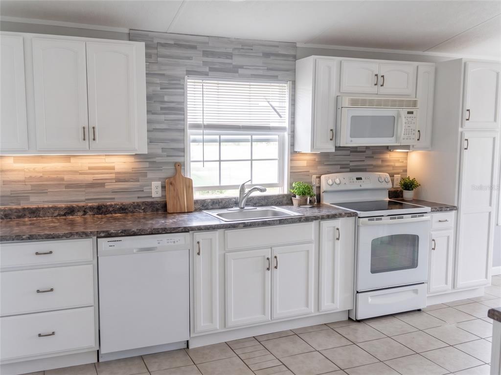 A kitchen features white cabinets, a dark laminate countertop, a tiled backsplash, and white appliances — 3296 LAKE BUFFUM ROAD W, FORT MEADE, FL