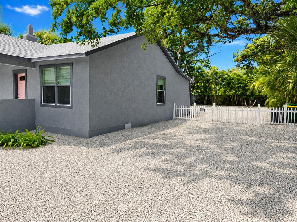 A gray stucco house exterior features a gravel driveway and a white picket fence — 1235 32ND STREET, SARASOTA, FL
