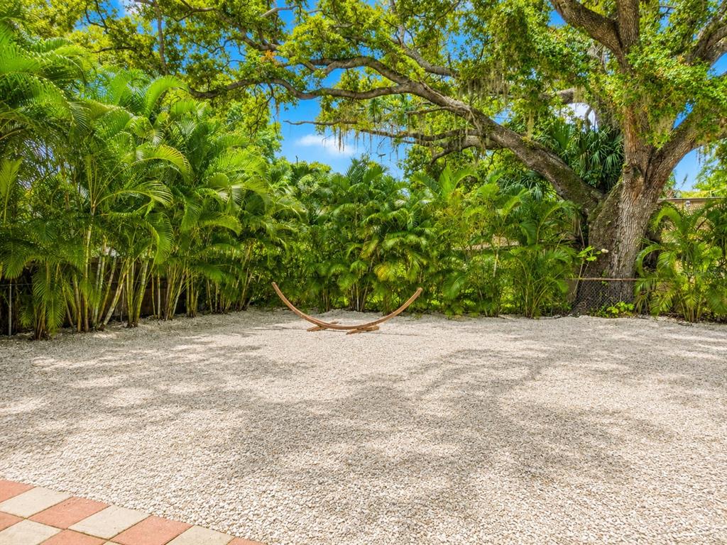 A gravel backyard features a hammock stand surrounded by palm trees and a large oak tree — 1235 32ND STREET, SARASOTA, FL