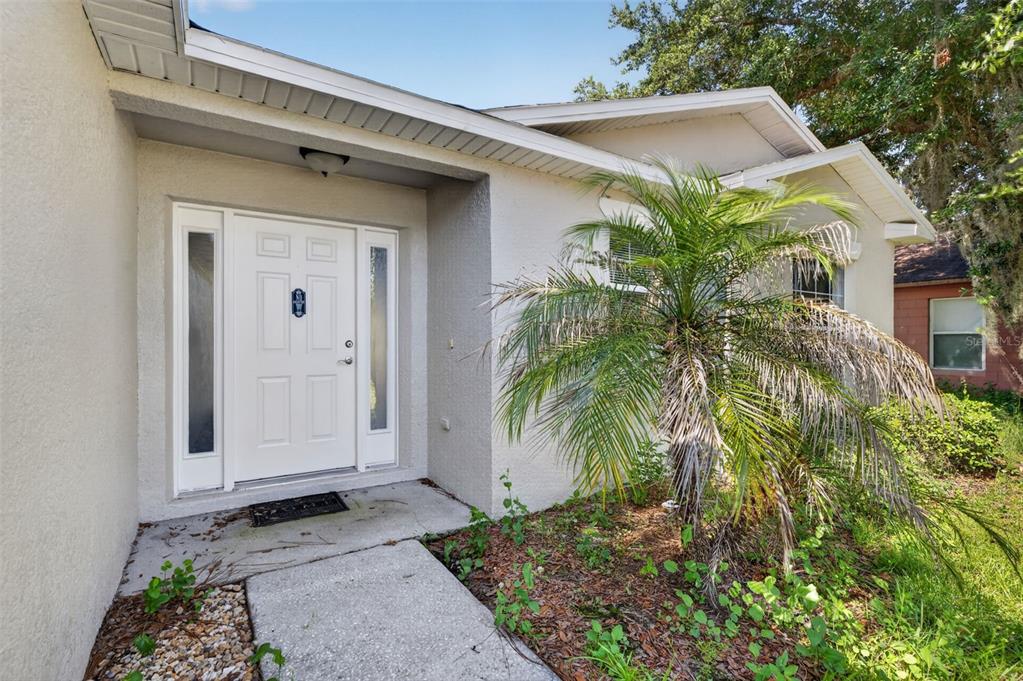 The exterior of a house features a white front door with sidelights and a palm tree — 719 WAXWING COURT, POINCIANA, FL