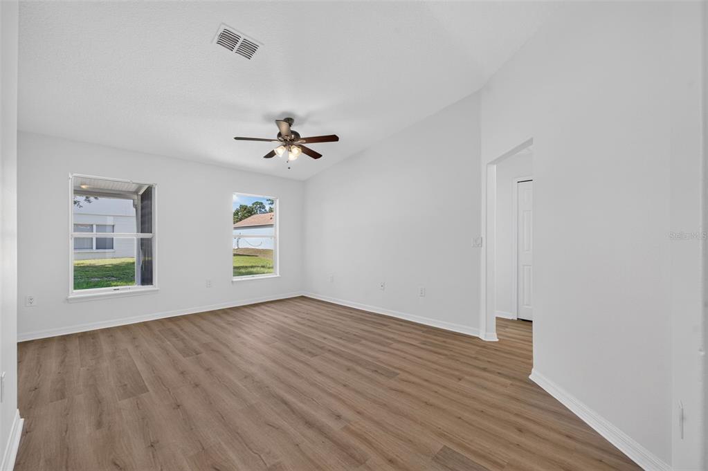 An empty room with light wood-look flooring, white walls, a ceiling fan, and two windows — 719 WAXWING COURT, POINCIANA, FL