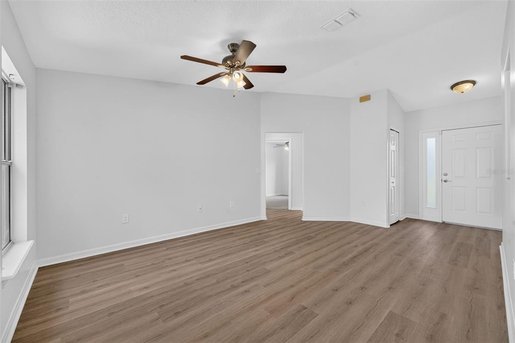 An empty room with light gray walls, wood-look flooring, a ceiling fan, and an entryway — 719 WAXWING COURT, POINCIANA, FL