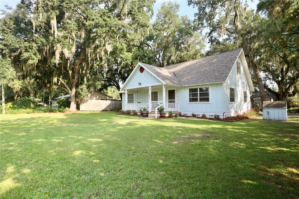A light blue cottage with a front porch sits on a large, grassy, tree-shaded lot — 4849 MEADOW DRIVE, ST CLOUD, FL