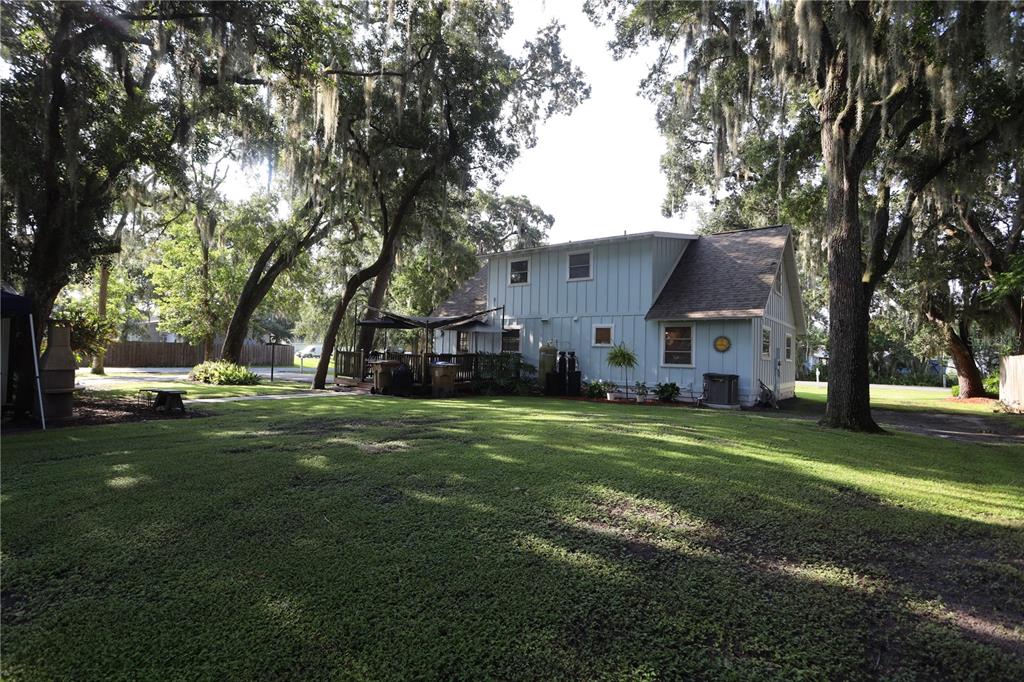A light blue two-story house with a wooden deck sits on a grassy, tree-shaded lot — 4849 MEADOW DRIVE, ST CLOUD, FL