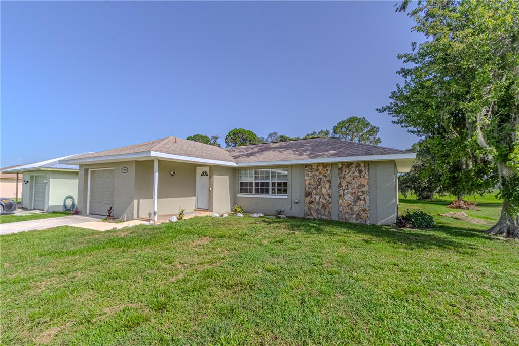 A single-story house with a stone facade, a garage, and a large grassy front yard — 7208 HONEYSUCKLE DRIVE, SEBRING, FL