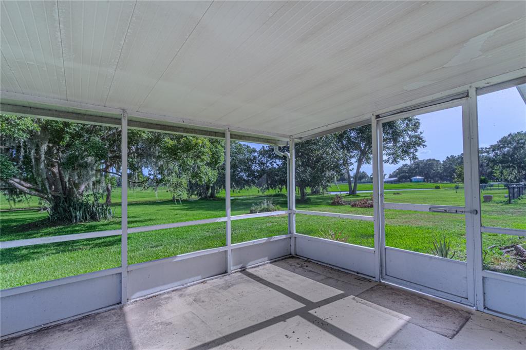 A screened-in porch with a concrete floor overlooks a grassy yard with large trees — 7208 HONEYSUCKLE DRIVE, SEBRING, FL