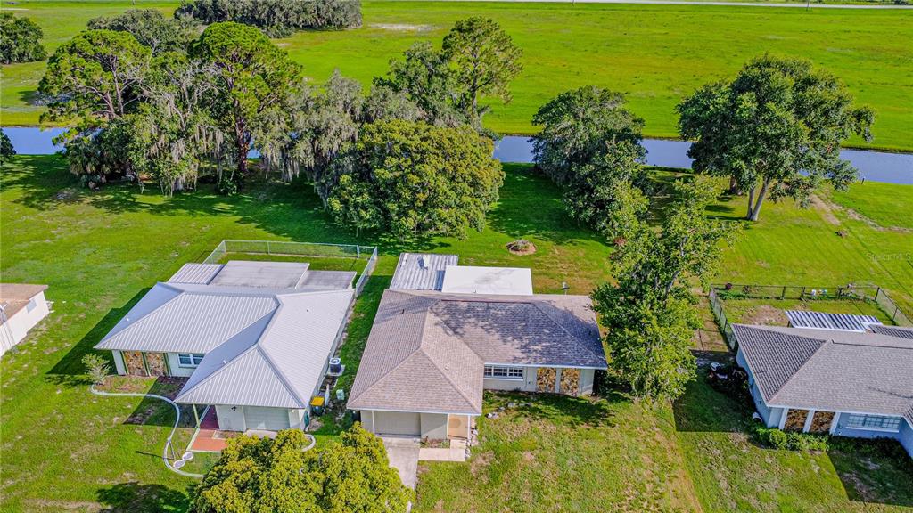 An aerial view shows three houses with metal and shingle roofs near a canal — 7208 HONEYSUCKLE DRIVE, SEBRING, FL