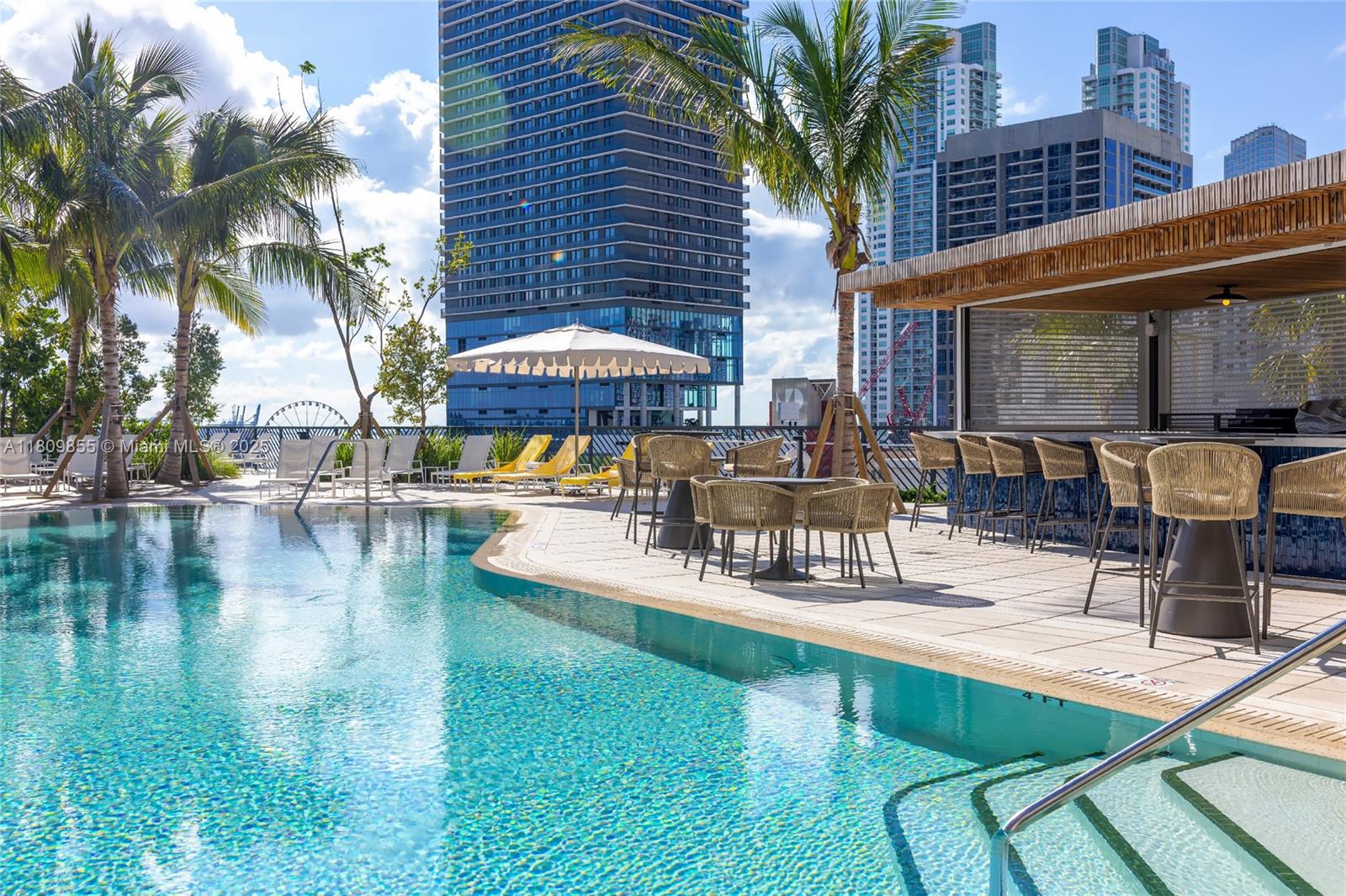 An outdoor swimming pool area features lounge chairs, tables with chairs, and a bar counter — 159 NE 6th St # 3012, Miami FL 33132, MIAMI, FL