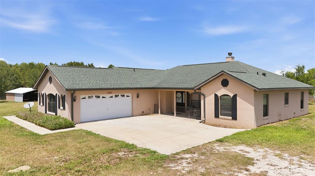 A single-story house with a green roof, tan stucco exterior, and an attached two-car garage — 14433 LAKE YALE ROAD, UMATILLA, FL