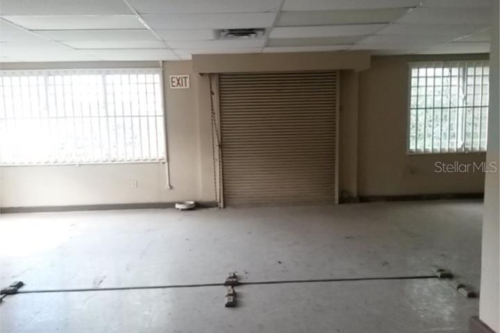 An empty commercial room features a roll-up metal door, barred windows, and a drop ceiling — 11 VELA ST., SAN JUAN, PR