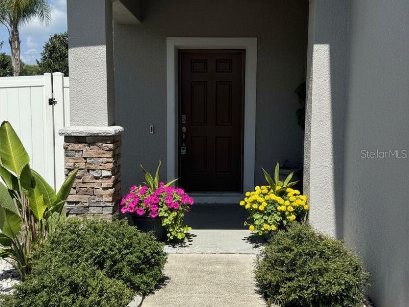 A dark brown front door is flanked by potted flowers and shrubs under a covered entryway — 1010 ATLANTIC AVENUE, FRUITLAND PARK, FL