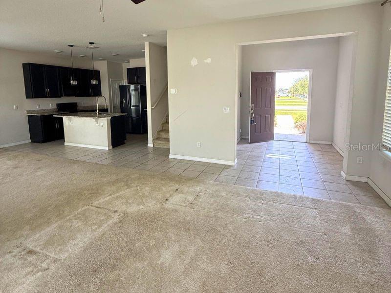 An open-concept living area features a carpeted floor, a tiled kitchen, and a front entryway — 1010 ATLANTIC AVENUE, FRUITLAND PARK, FL