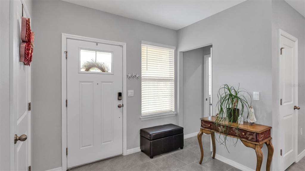 An entryway features a white front door, a window with blinds, a bench, and a table — 12003 HOLYSTONE STREET, WINTER GARDEN, FL