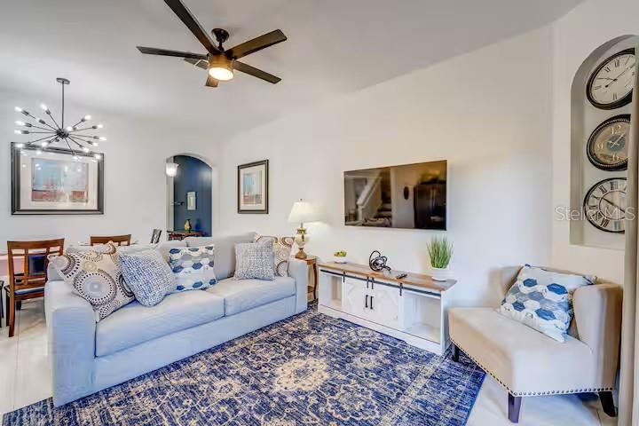 A living room features a blue patterned rug, a light-colored sofa, and wall-mounted clocks — 142 CAPRI DRIVE, DAVENPORT, FL