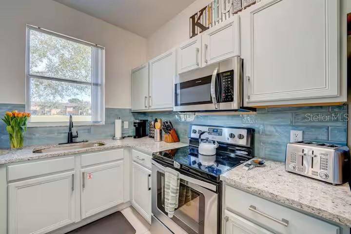 A kitchen features white cabinets, stainless steel appliances, a granite countertop, and a blue backsplash — 142 CAPRI DRIVE, DAVENPORT, FL