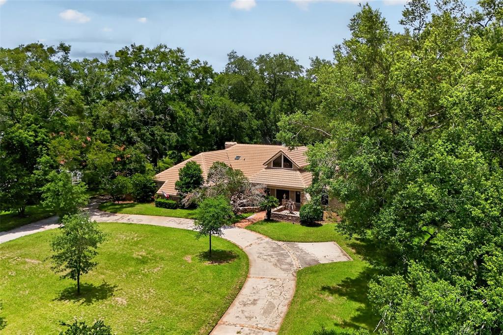 An aerial view shows a house with a tan roof surrounded by many large trees — 1808 WINGFIELD DRIVE, LONGWOOD, FL