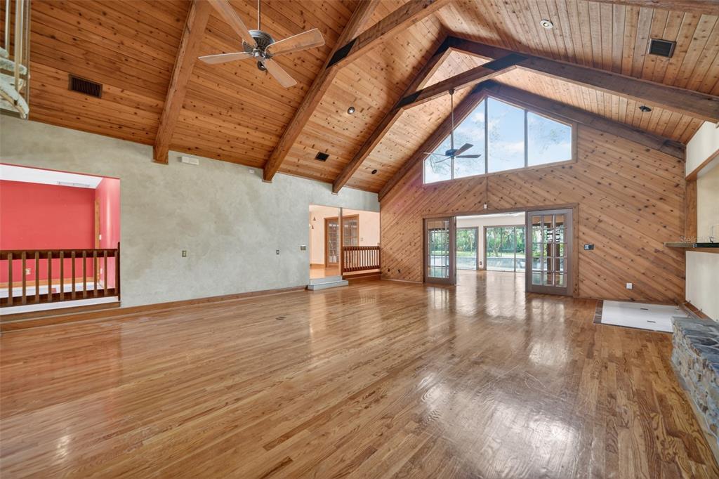 A spacious living room features vaulted wood-paneled ceilings, hardwood floors, and large glass doors — 1808 WINGFIELD DRIVE, LONGWOOD, FL