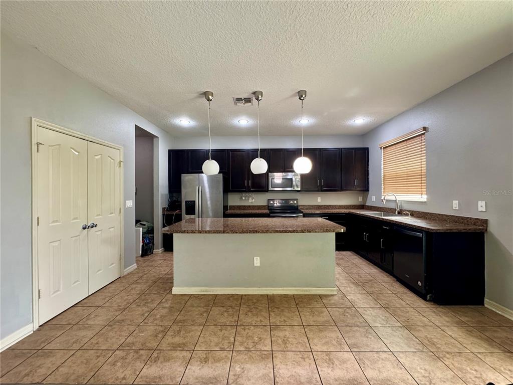 A kitchen features dark cabinets, granite countertops, a central island, and three pendant lights — 998 HERMOSA WAY, KISSIMMEE, FL