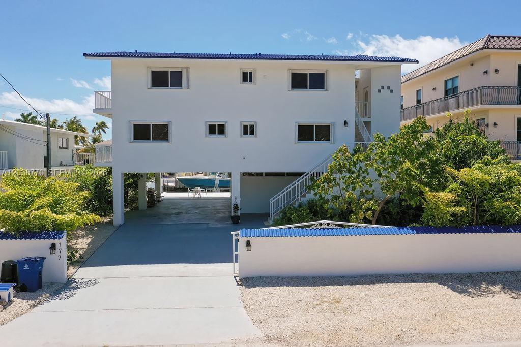 A white two-story house with a blue roof stands behind a low wall and driveway — 177 Lorelane Pl, Key Largo FL 33037, KEY LARGO, FL