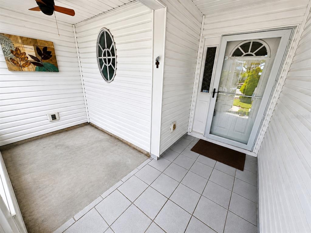 A covered porch features a concrete floor, tiled entryway, white siding, and a glass storm door — 3526 INNISBROOK DRIVE, LAKELAND, FL
